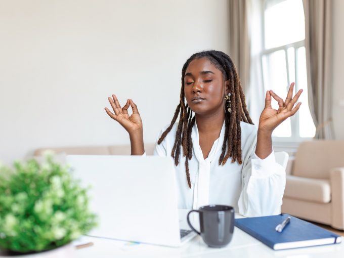 Calm African female executive meditating taking break at work for mental balance, mindful businesswoman feeling relief and no stress doing yoga at work ignoring avoiding stressful job